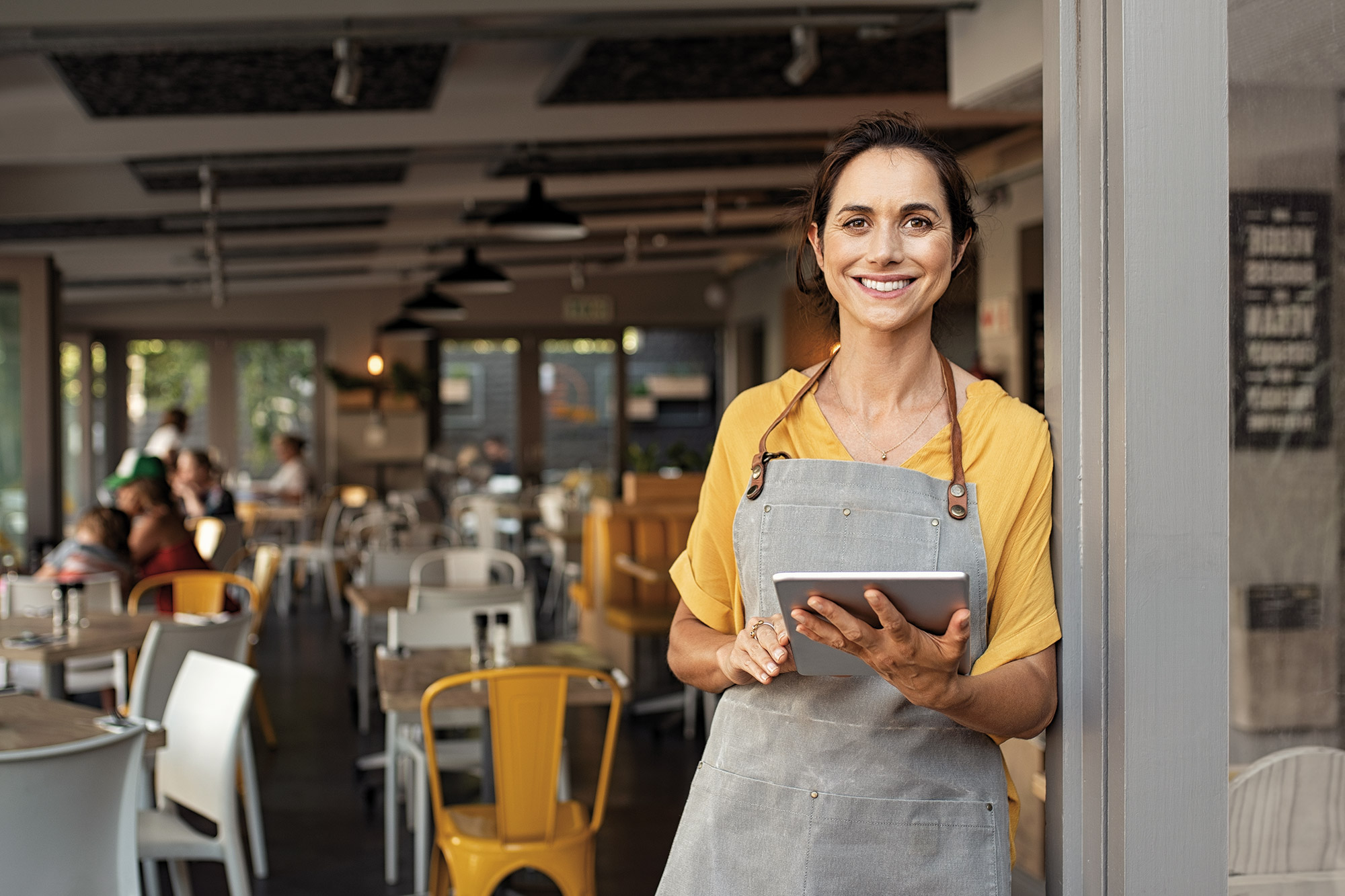 Eine Frau mit einem Tablet in der Hand steht am Eingang eines Cafés
